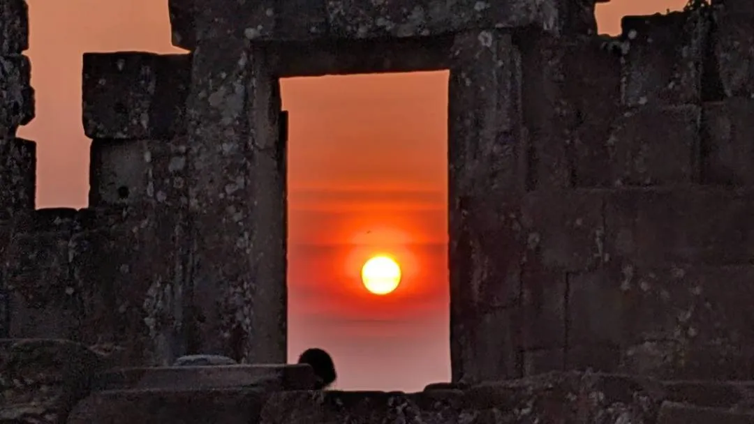 A red sun sets through a ruined temple window