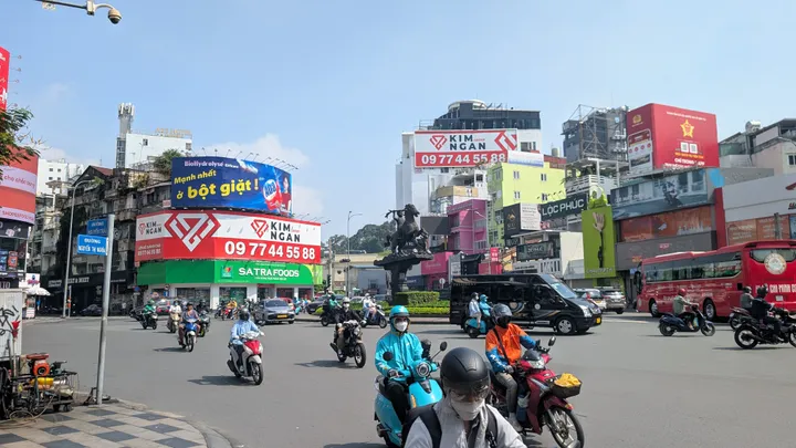 A junction in Ho Chi Minh City with a statue in the centre and people on scooters driving by