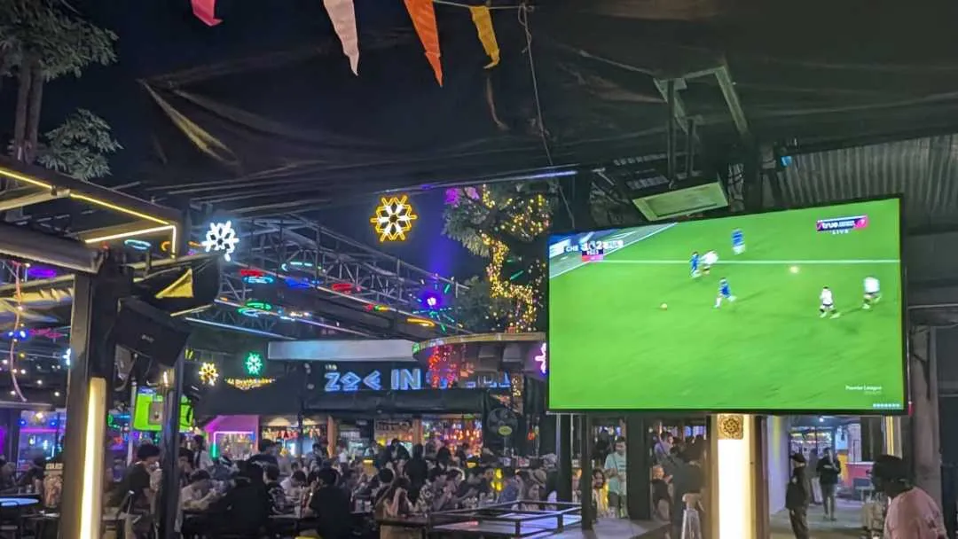 A TV screen showing a football game in an outdoor bar at night