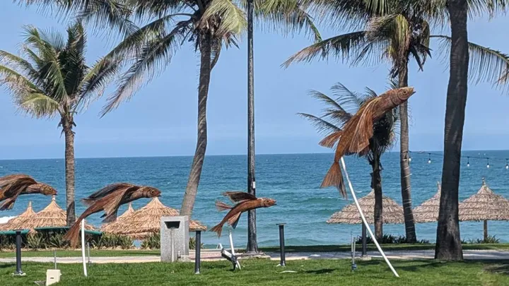 A beach with palm trees with the sea in the background and fish sculptures