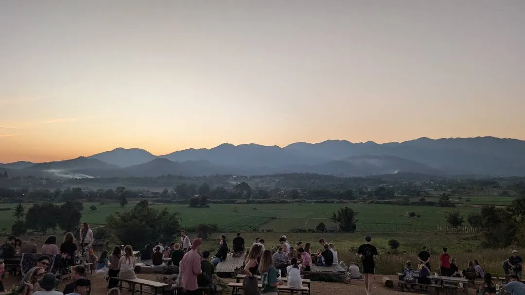 Sun setting over a mountain while a crowd on a hill looks on