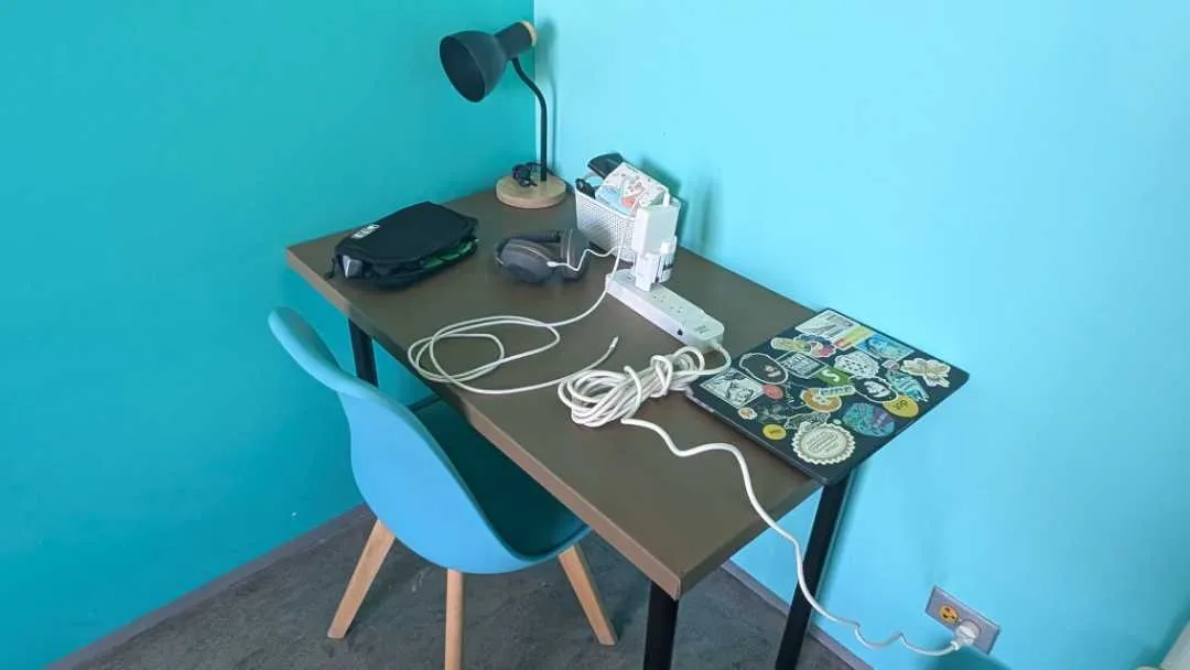 A busy desk with laptop, lamp and wires on it