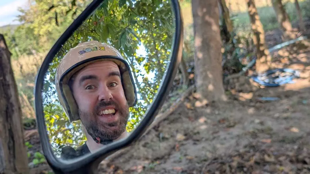 A handsome man looking at his reflection in the mirror of a scooter