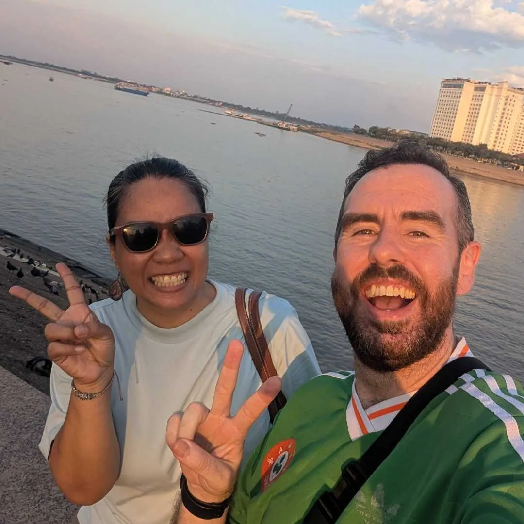 Two people taking a selfie with a river behind them in Phnom Penh