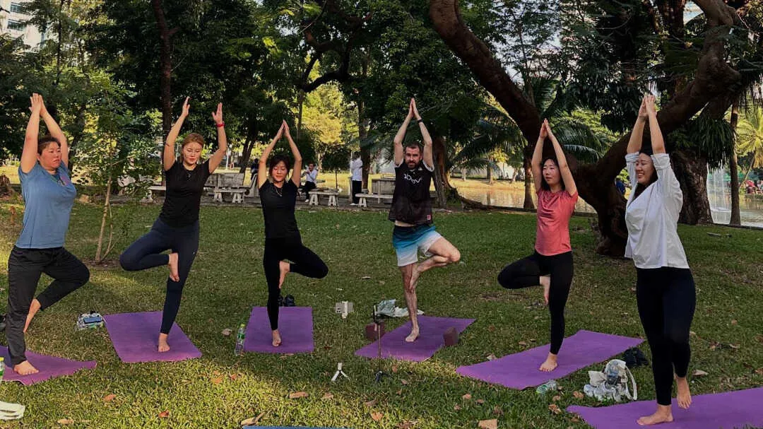 One fella and 5 women doing a yoga pose in a park