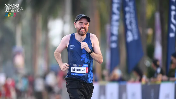 A man running the Da Nang Marathon smiling as he nears the end of a race