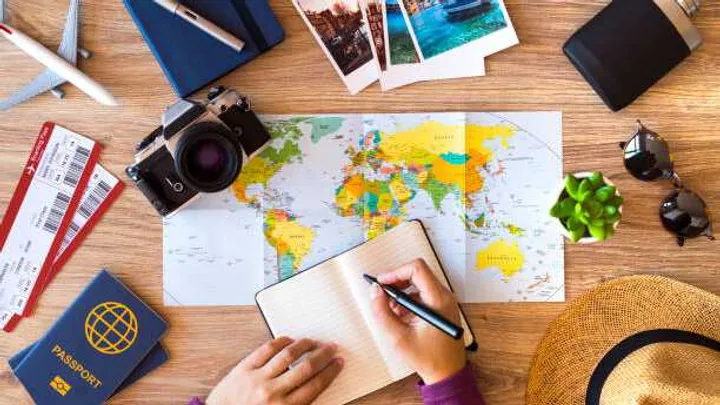 A plan view of a desk full of items for planning a trip such as a map, notepad, passport, camera