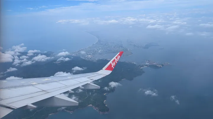 A picture looking out the window of an aeroplane. The wing can be seen with Da Nang in the background